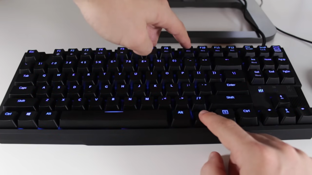 man’s hands typing on a keyboard with blue lights