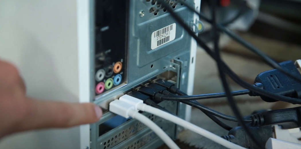 Hand pointing at wires connected to the back of a computer.