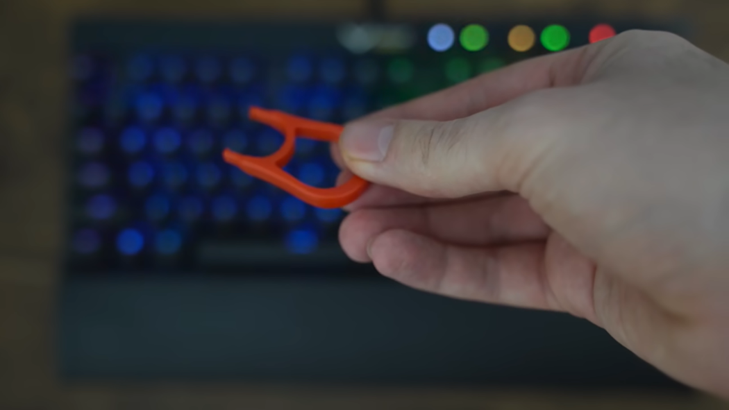 hand holding plastic red strainer in front of the keyboard
